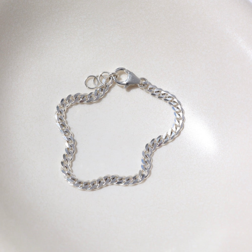 925 sterling silver cuban style chain link bracelet, laid out on a curvy ceramic dish