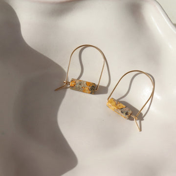 14k gold fill Leopard Skin Jasper Arches placed on a white plate in the sunlight. These earrings feature a hoop like earring with e leopard jasper stone attached to it.