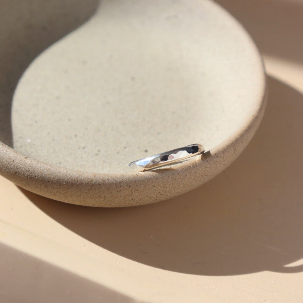925 sterling silver heritage band sitting on a gray plate in the sunlight. The heritage band Features a lightly hammered band to a high shine.