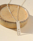 A silver hand-stamped, area code necklace with a delicate chain. Displayed on a small dish against a cream backdrop. 