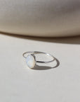 mother of pearl stone set in a bezel on a 925 sterling silver skinny ring band, photographed on a table next to a white ceramic dish in the sun