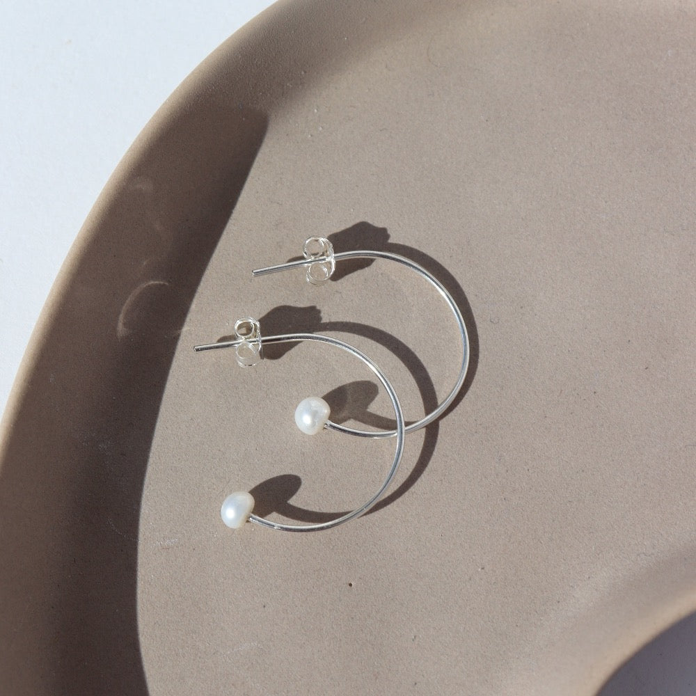 925 sterling silver Balanced Pearl Hoops laid on a tan plate in the sunlight.