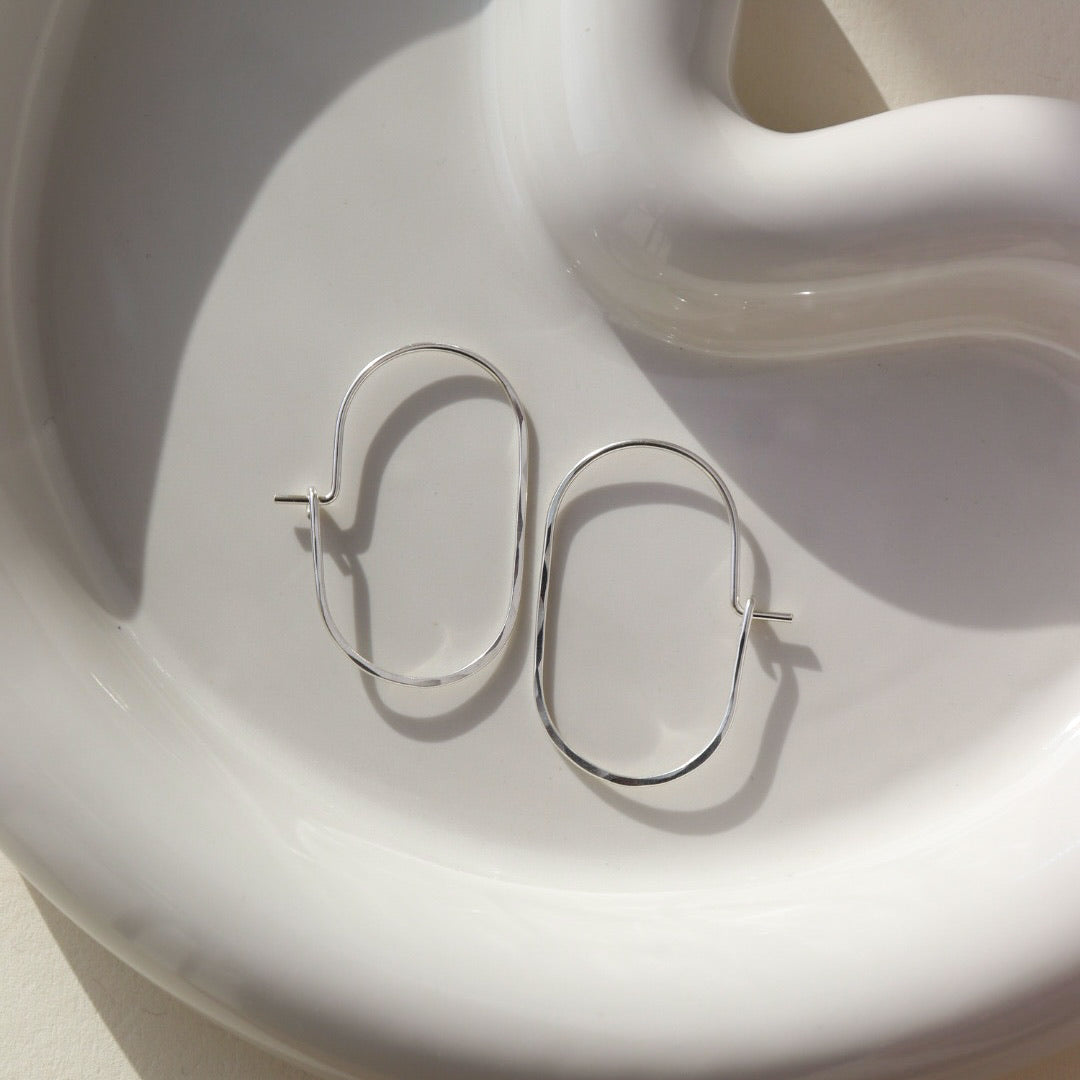 925 sterling silver capsule hoops laid on a white plate. Handmade in Eau Claire, Wisconsin.