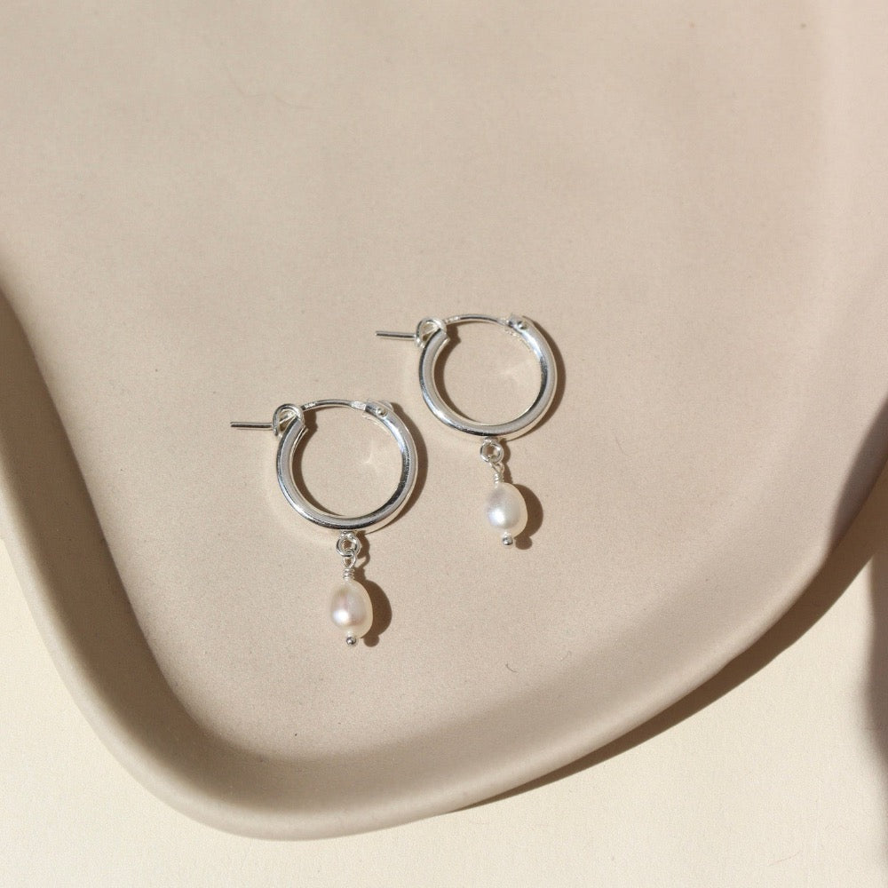 14k gold fill classic pearl hoops laid on a white plate in the sunlight.