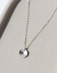 a sterling silver necklace featuring a dainty chain and a small, concave, polished disc