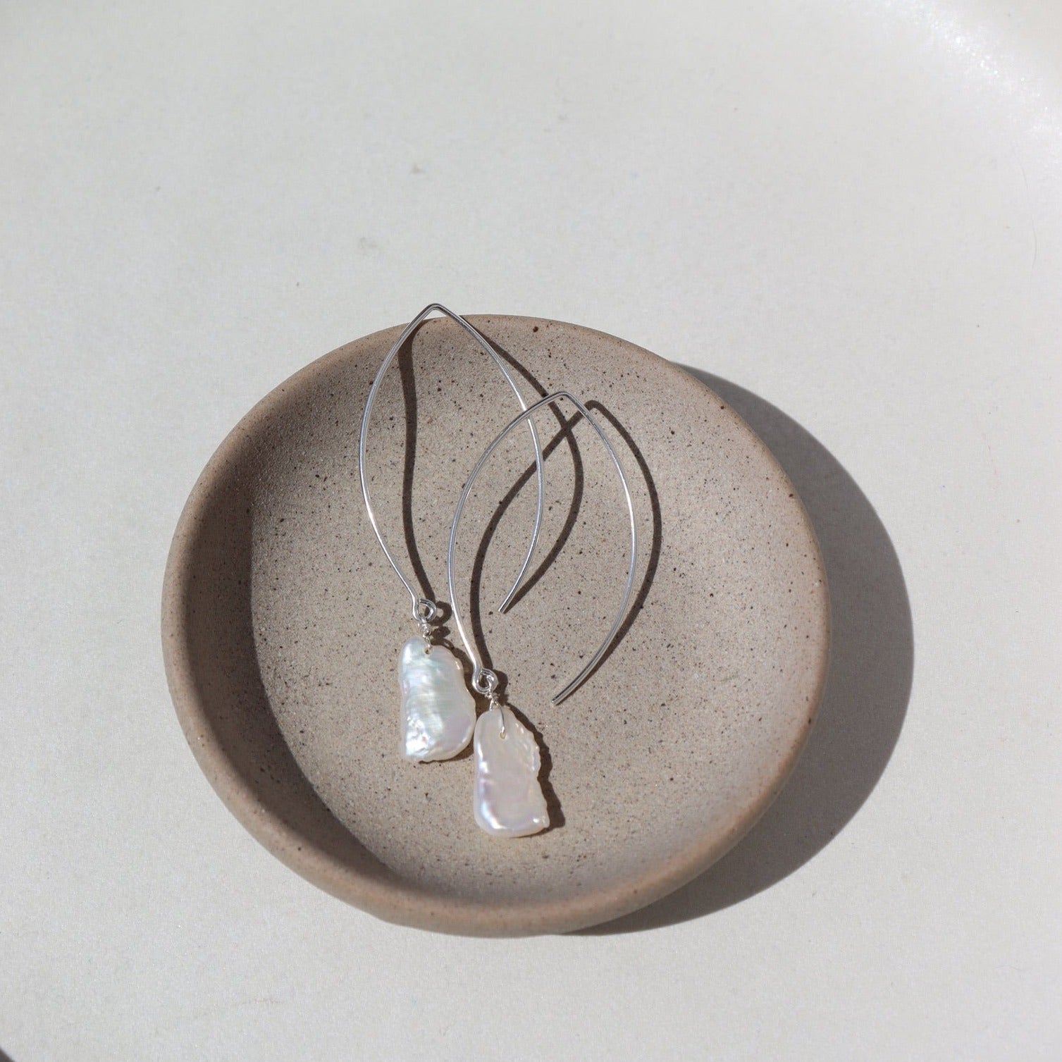 14k Gold fill Juno Earrings laid on a tan plate in the sunlight. Perfect for your wedding fits.