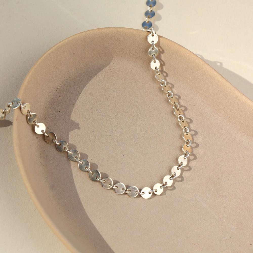 925 sterling silver Starlight Choker laid in the sunlight on a gray plate. This choker is perfect for layering. This Necklace features circle disc that are linked together.