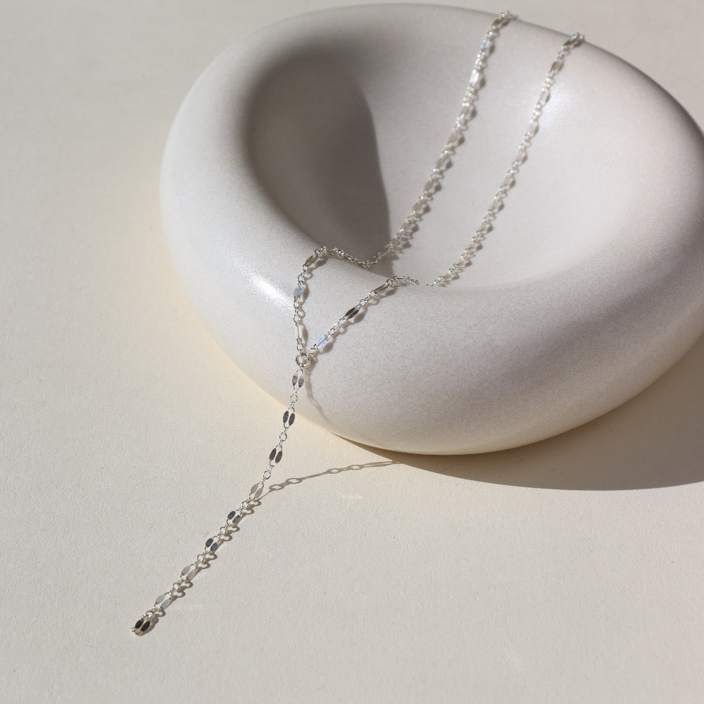 sterling silver lariat chain, photographed on a cream colored ceramic dish