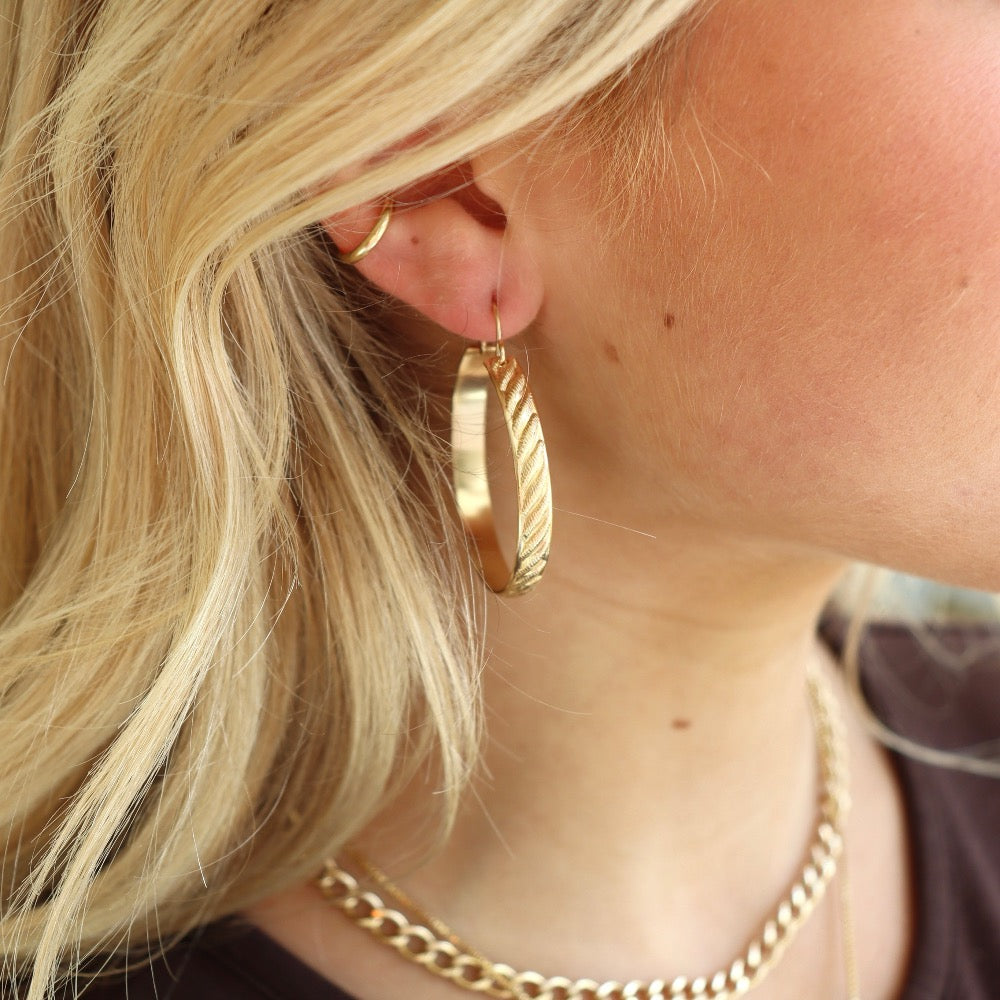 Patterned gold hoops leaning on a beige tray handmade by Token Jewelry in Eau Claire, WI