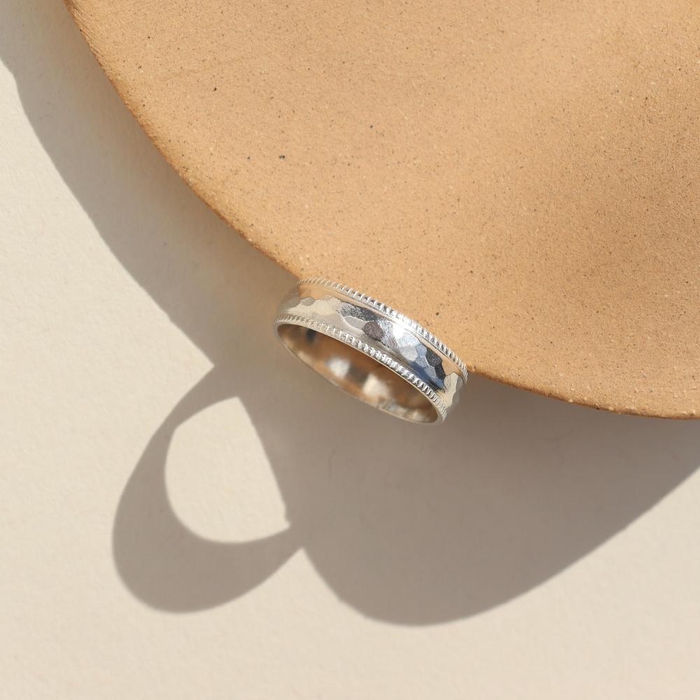 A silver hammered band with rippled edges. Displayed on a small ring dish. 
