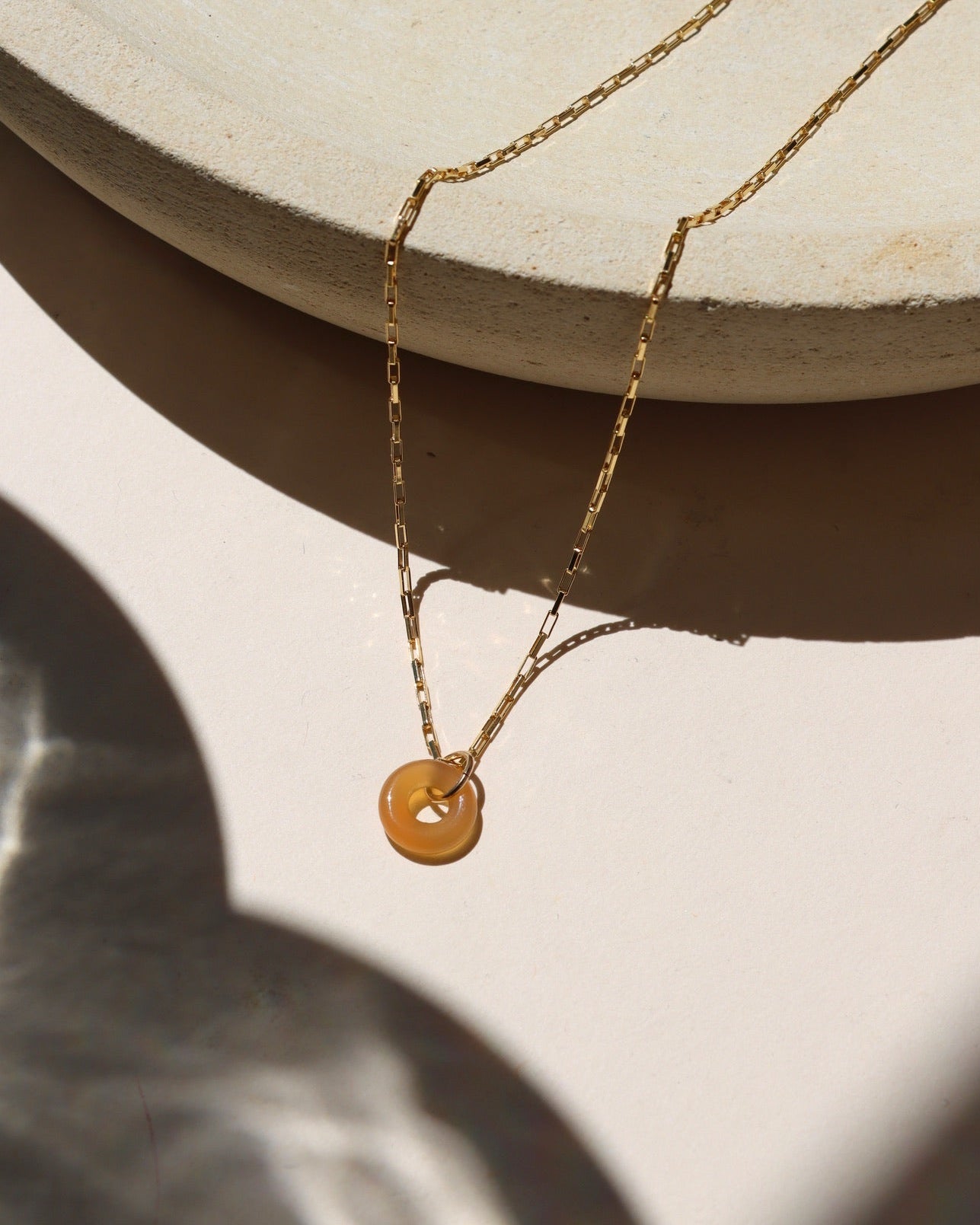 Agate donut shaped gemstone pendant attached to a 14k gold Fill chain in the sunlight
