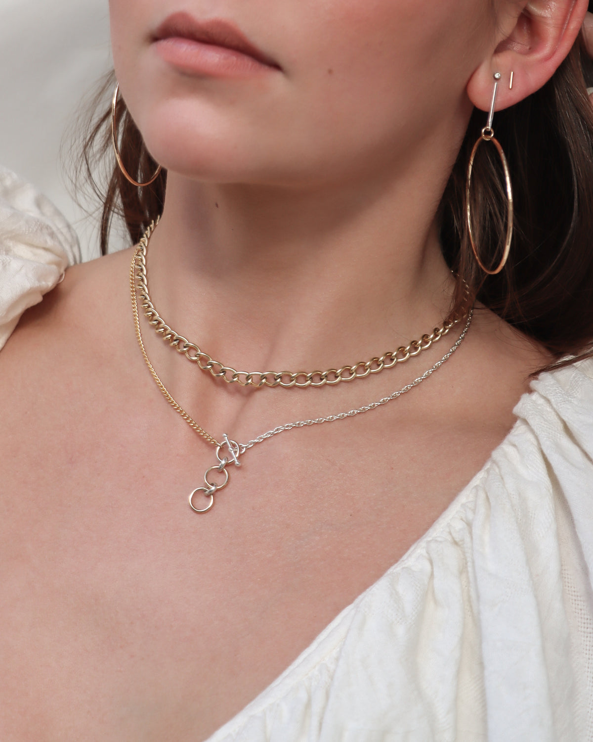 Model wearing mixed metal Alloy Toggle Necklace with gold and silver chains and dangling circle accents, layered with a gold chain necklace and paired with Alchemy Hoops.