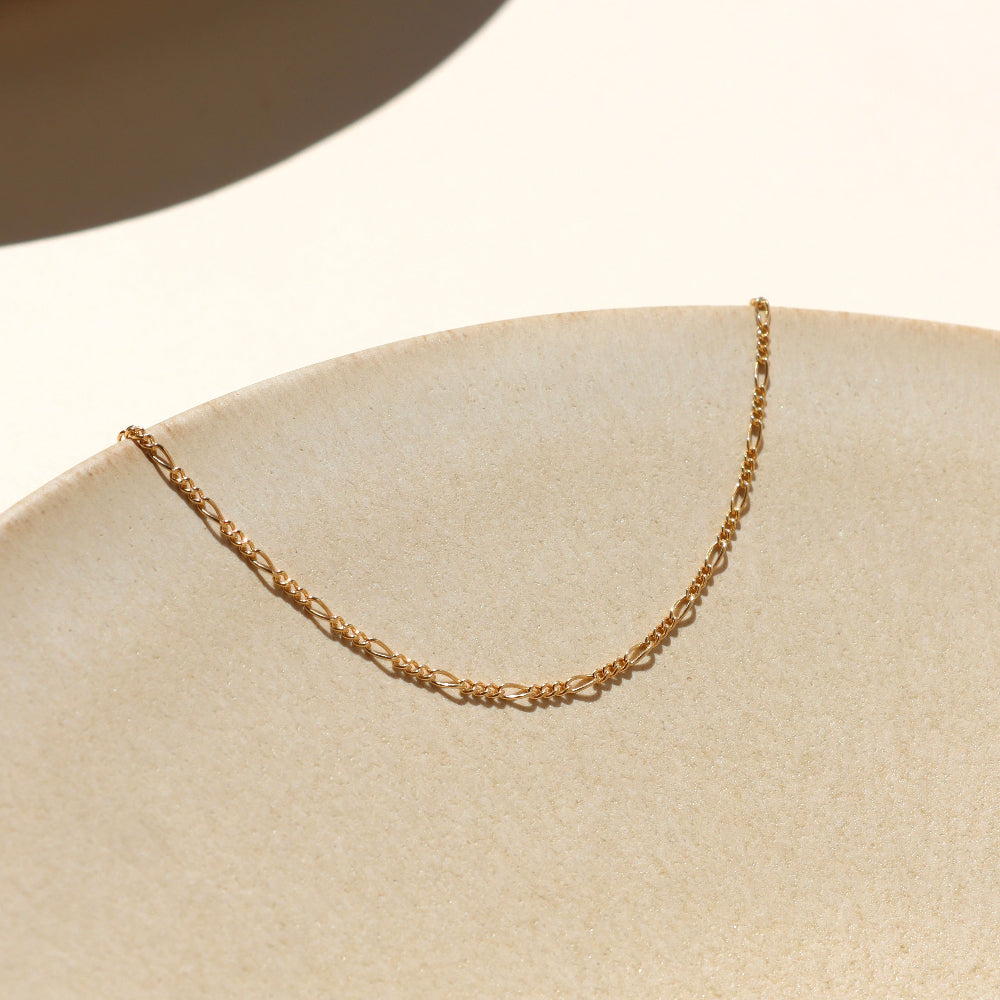 14k gold fill delicate figaro chain bracelet on a light surface