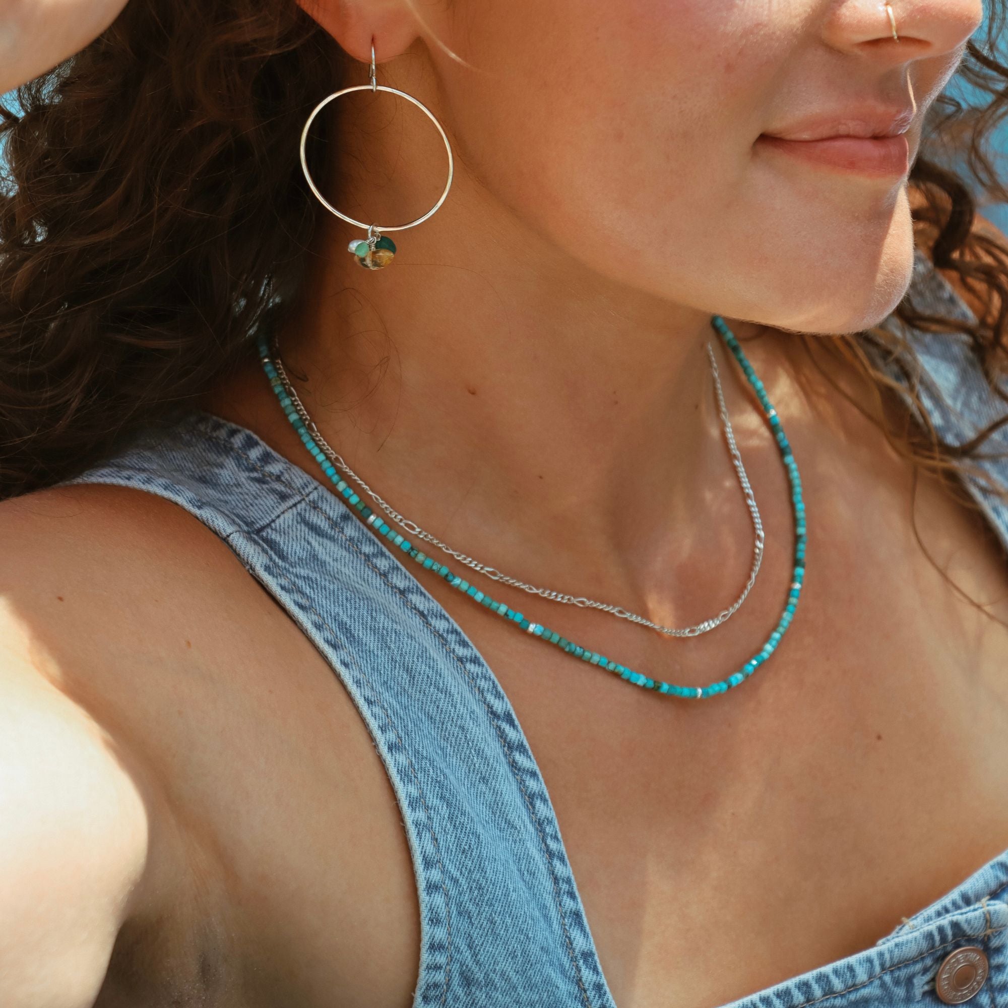 Model wearing a sterling silver figaro chain stacked with a turquoise beaded necklace and gemstone charm earrings in the sunlight.