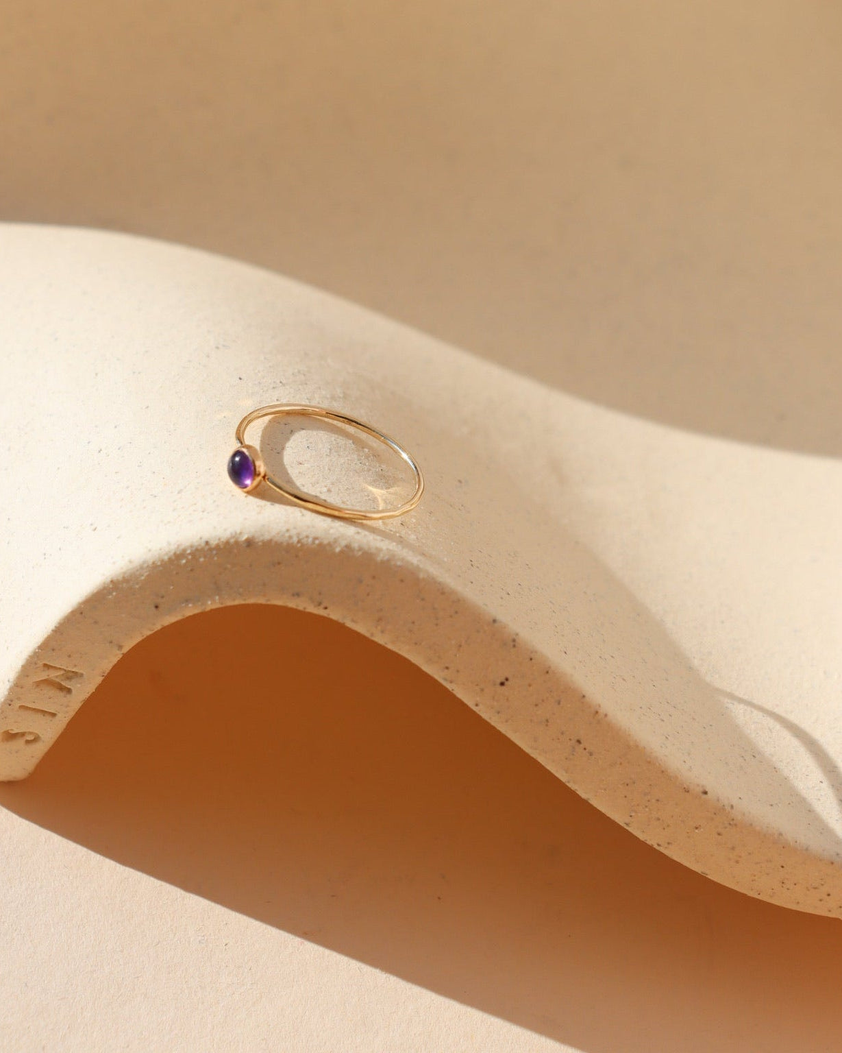 vibrant purple amethyst stone in a 14k gold fill bezel set ring on a wavy plate