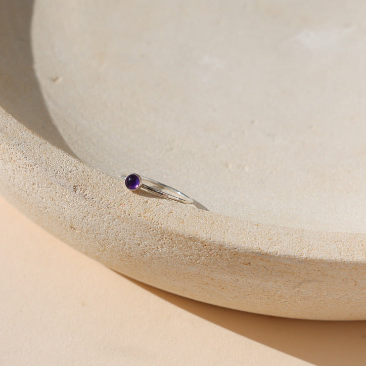 sterling silver band ring with 4mm amethyst stone on a light dish