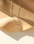 A sterling silver necklace featuring a thin standard chain with an open heart pendant anchored at the end. 