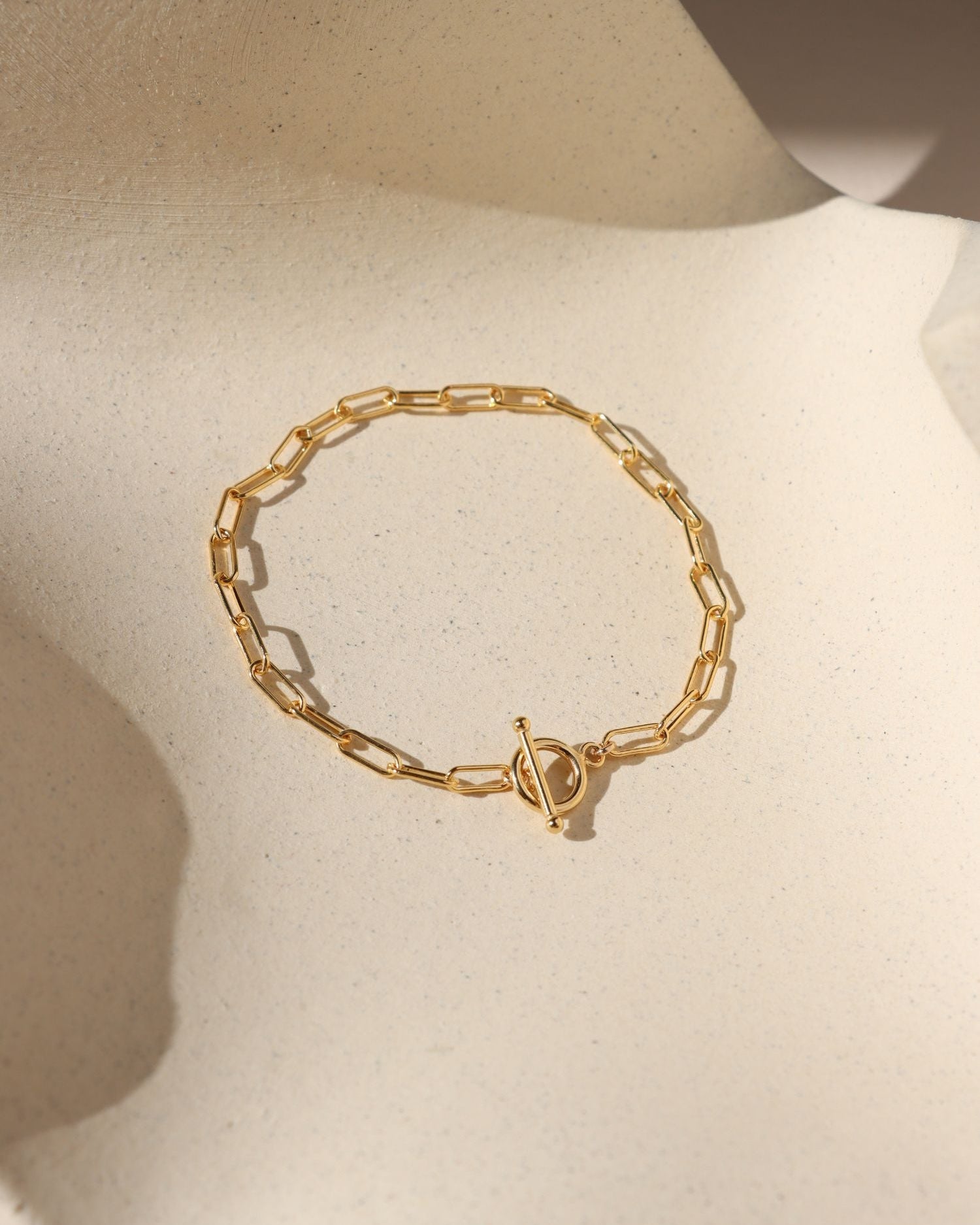 gold paperclip chain bracelet with toggle clasp in the sunlight on a light surface