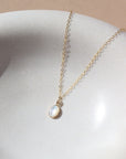 mother of pearl bezel pendant on a 14k gold fill delicate chain, photographed on a white ceramic dish