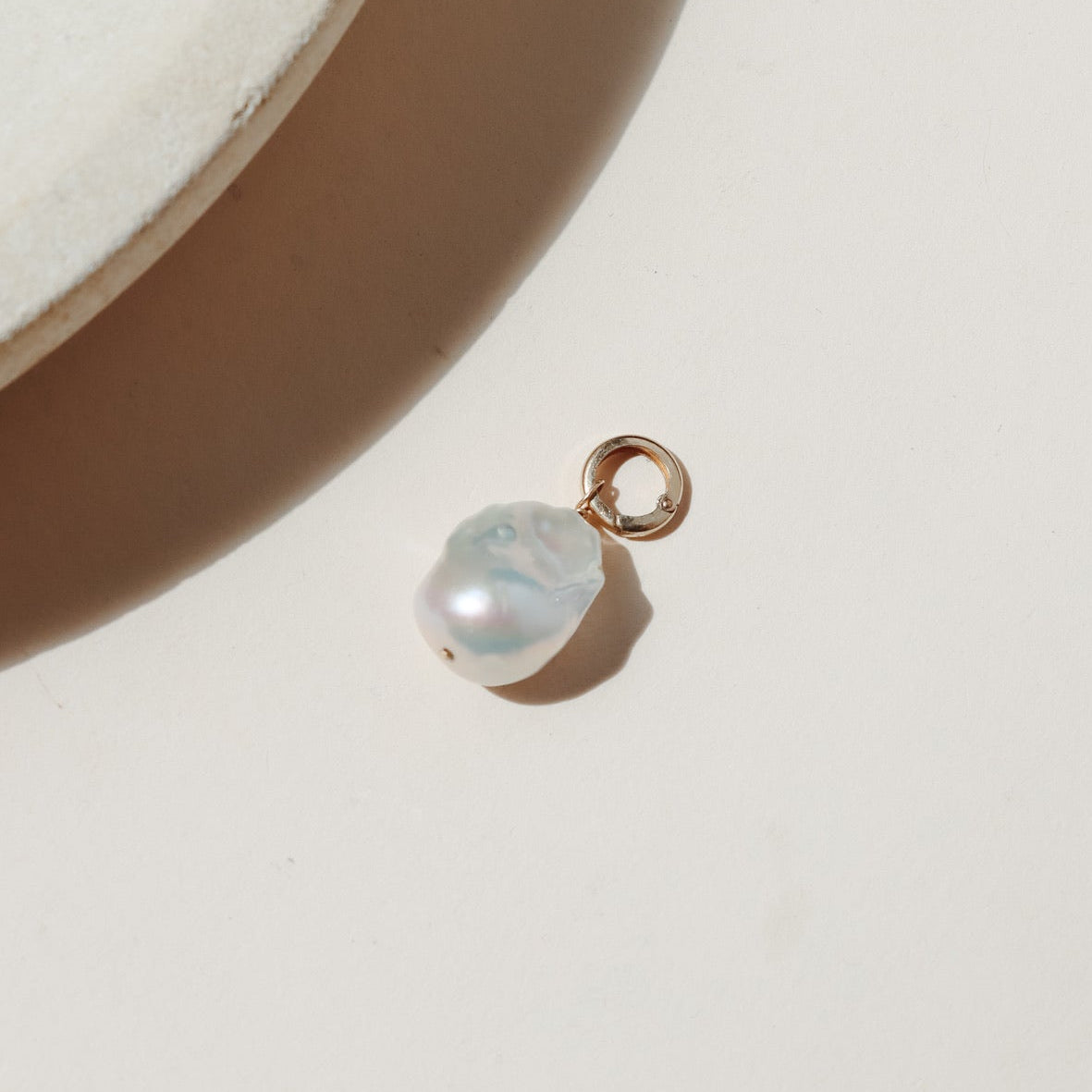 Large freshwater pearl on a round gold fill connector laid on a beige background in the sunlight