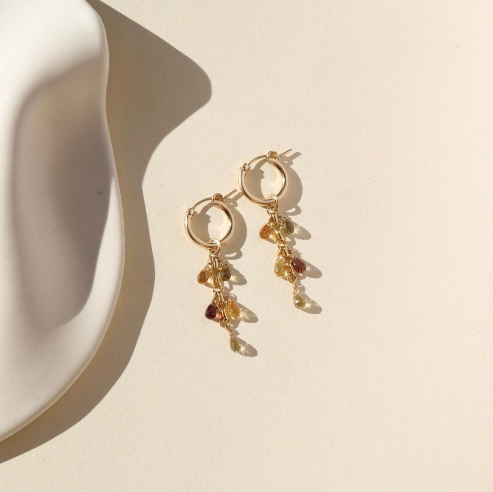 Small gold hoops with 5 zircon faceted teardrop stones on each earring. Earrings are displayed on cream backdrop. 