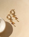 Small gold hoop with 5 zircon faceted teardrop stones on each earring. Earrings are displayed on tan dish. 