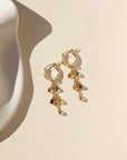 Small gold hoops with 5 zircon faceted teardrop stones on each earring. Earrings are displayed on cream backdrop. 