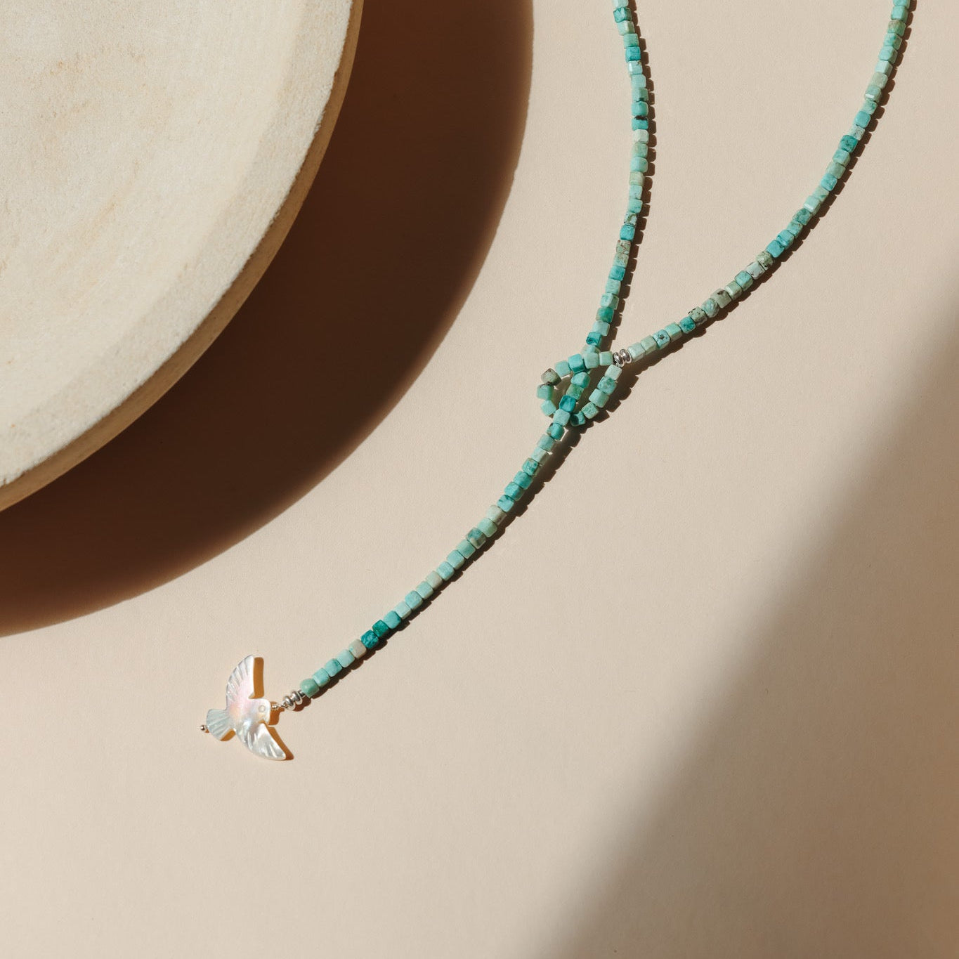 Turquoise beaded necklace with pearl bird charm on a light surface