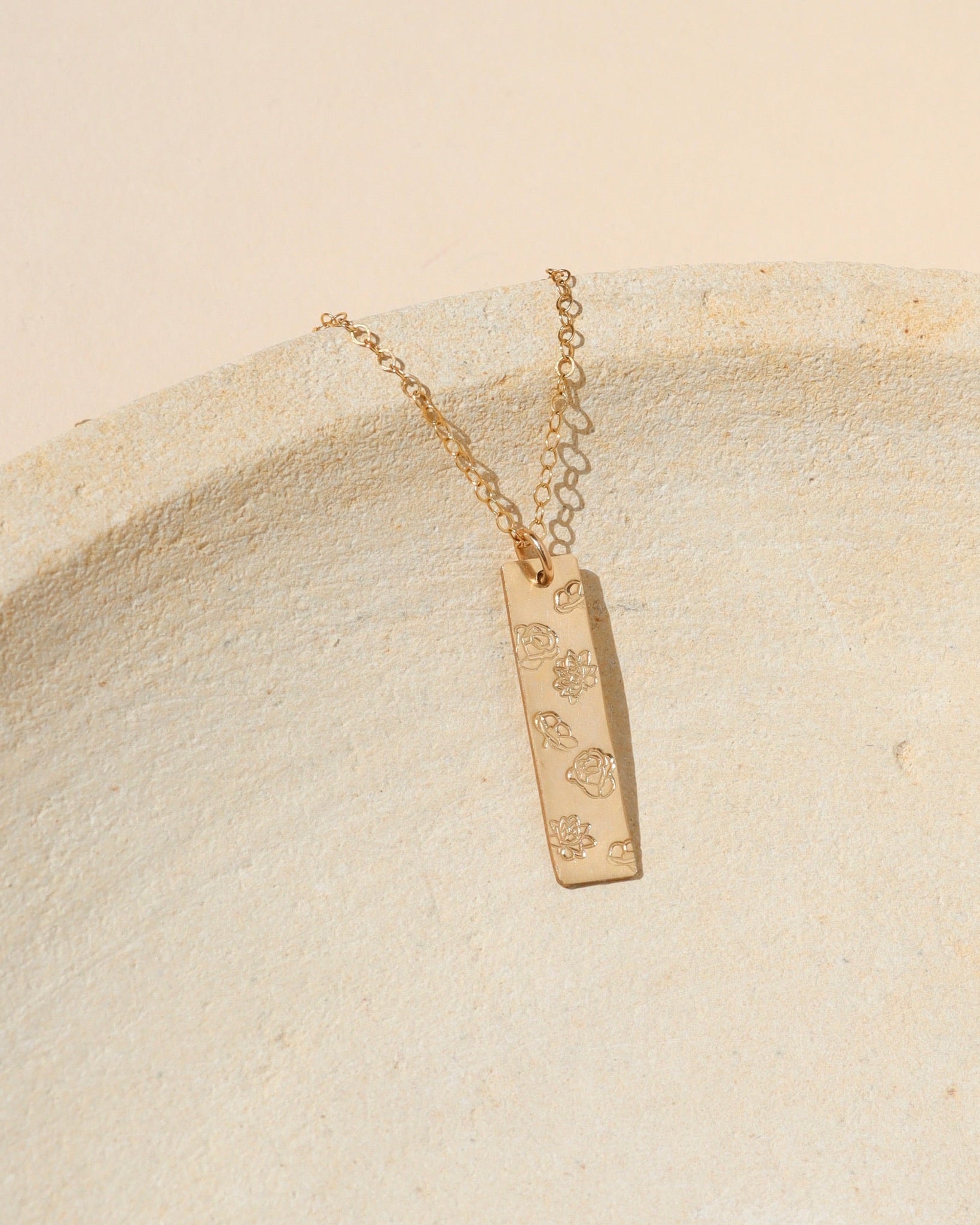 14k gold fill hand stamped bar pendant with flowers on a delicate chain on a light dish