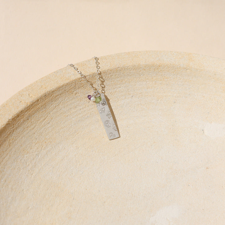 sterling silver delicate chain necklace with sterling silver hand stamped flower pendant on a light dish