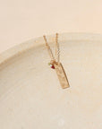 14k gold fill delicate chain necklace with hand stamped flowers on a bar pendant with birthstone charms on a light dish
