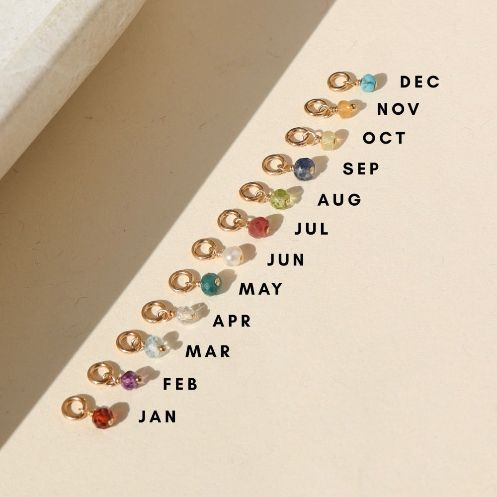 group of 14k gold fill jump rings with birth stone charms on a light surface