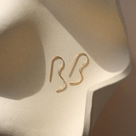 14k gold fill b shaped earrings on a light dish