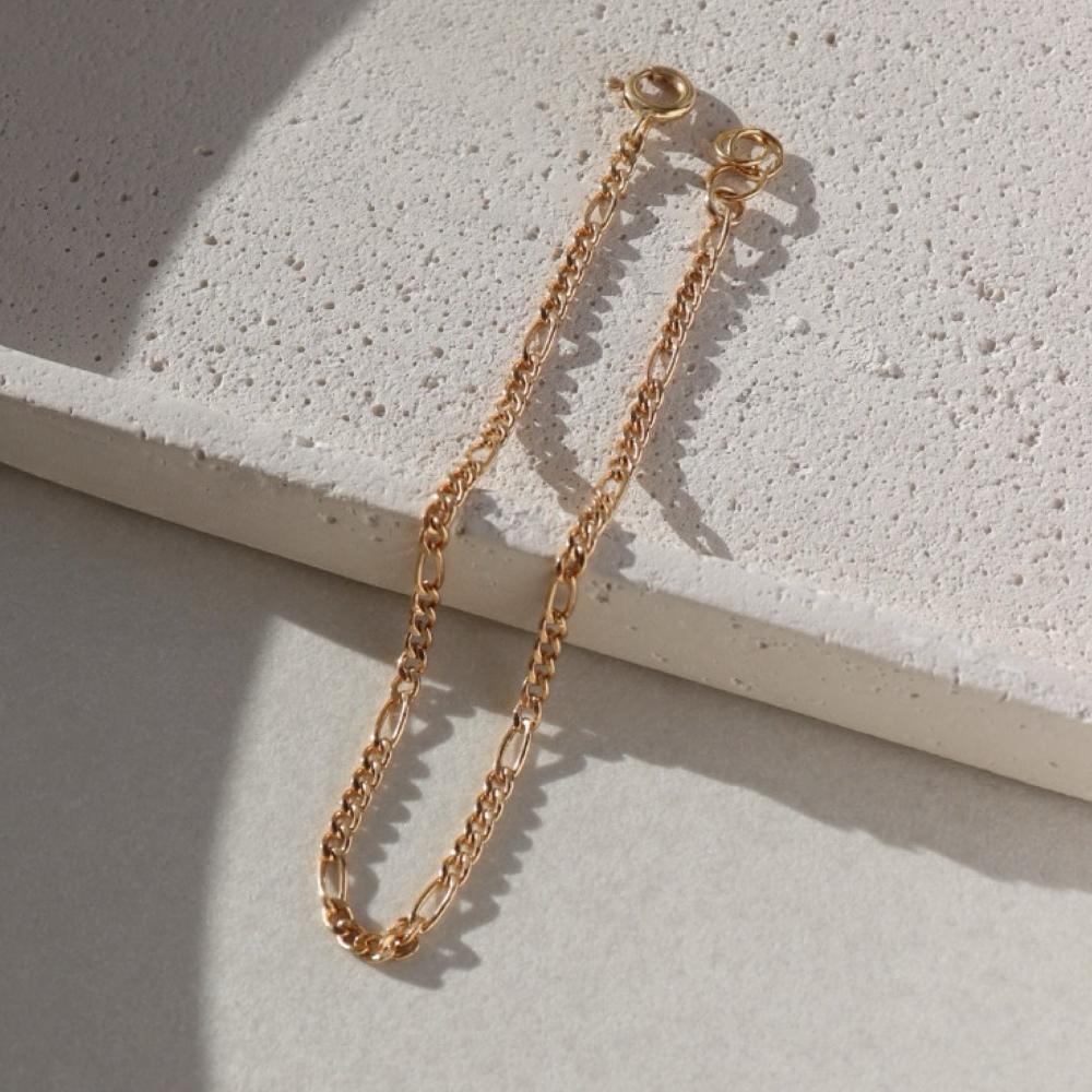 14k gold fill figaro chain bracelet on a light textured dish