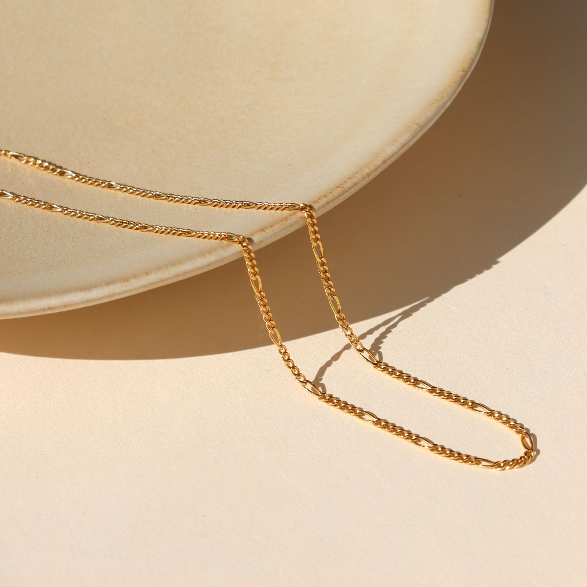 14k Gold Fill Figaro stacking chain on a light dish in the sunlight