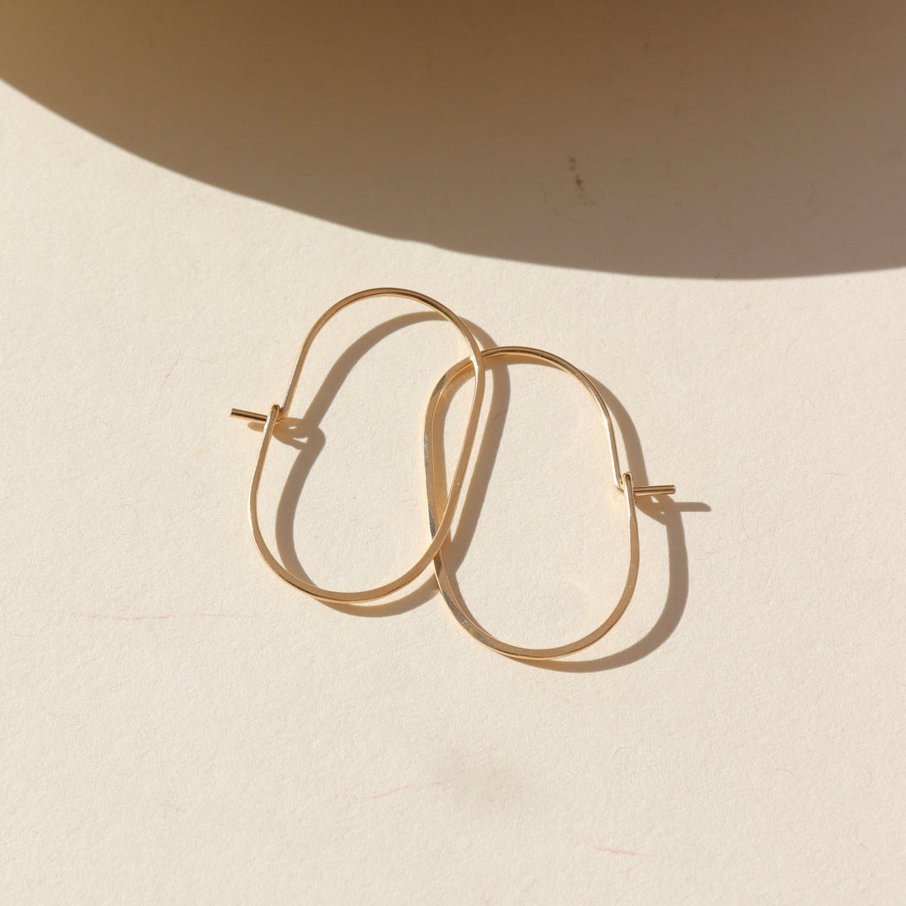 14k gold filled capsule hoops laid in the sun.