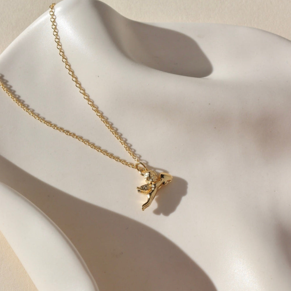 14k gold fill necklace with a thin standard chain with a cupid gold charm at the end of chain. Necklace is displayed on a white dish. 