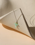 sterling silver delicate chain necklace with Chrysoprase Cross charm on a light dish
