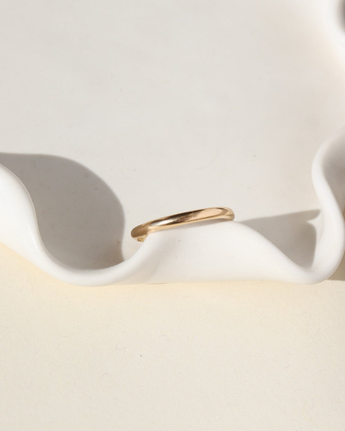 smooth 14k solid gold band ring on a white dish 