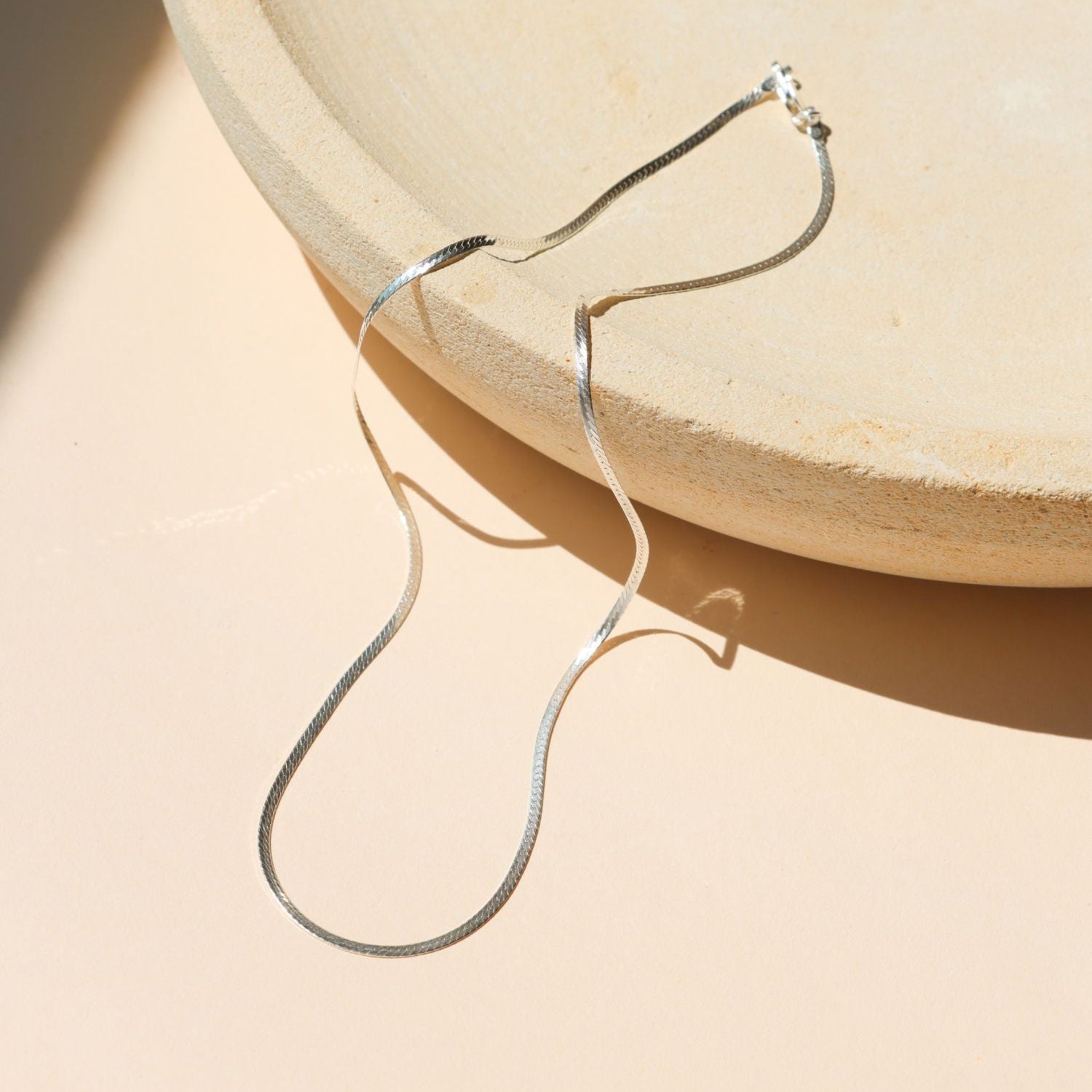 sterling silver herringbone chain necklace on a light dish in the sunlight