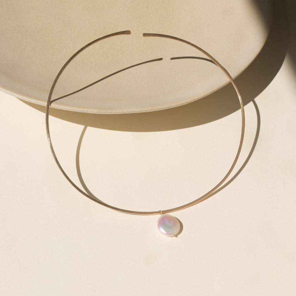 A 14k gold fill collarbone style necklace with a pearl dangling its center. 