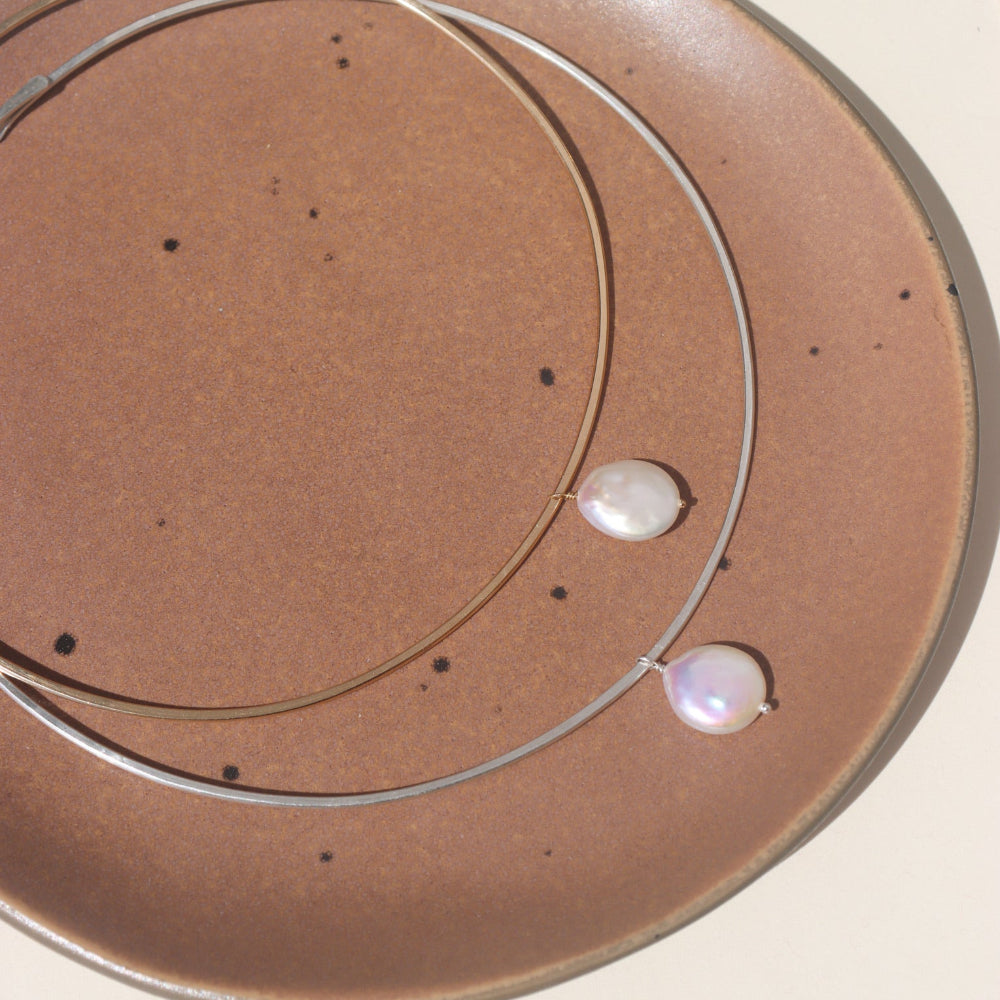 A collarbone style necklace with a pearl dangling at its center. 