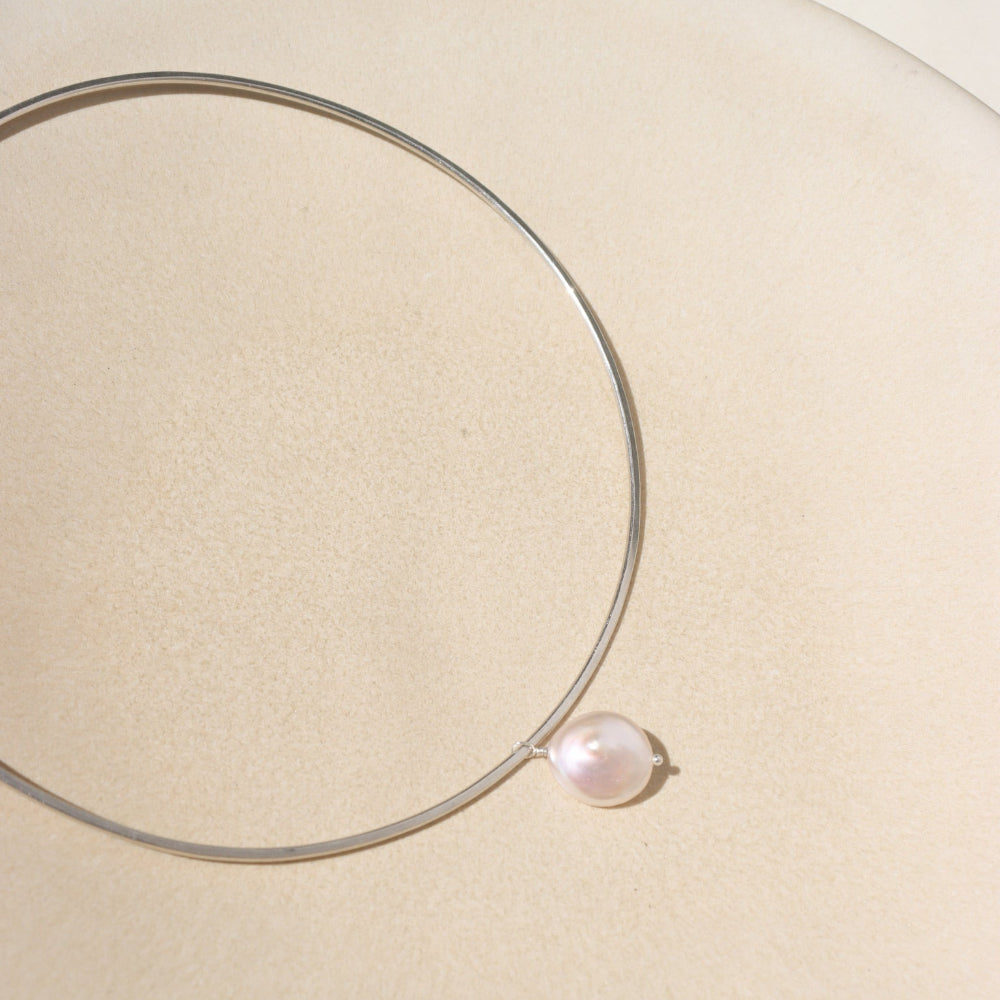 A sterling silver collarbone style necklace with a pearl dangling its center. 
