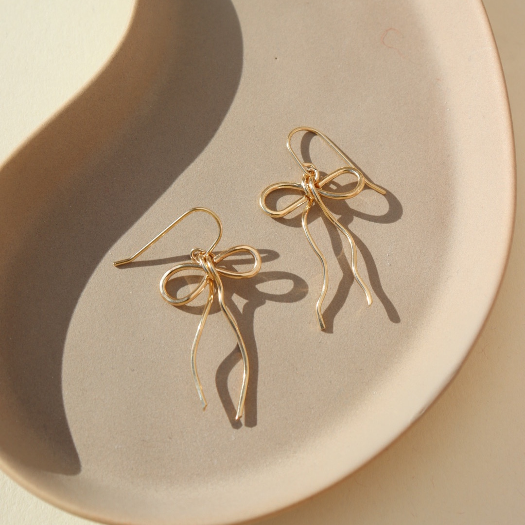 14k gold fill hand shaped bow earrings on french ear wire on a light dish