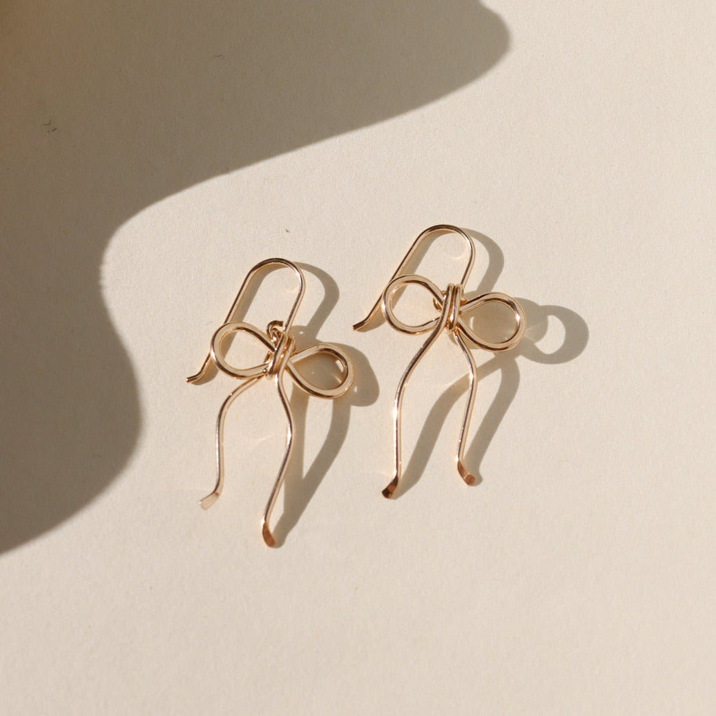 14k gold fill hand shaped bow earrings on french ear wire on a light background