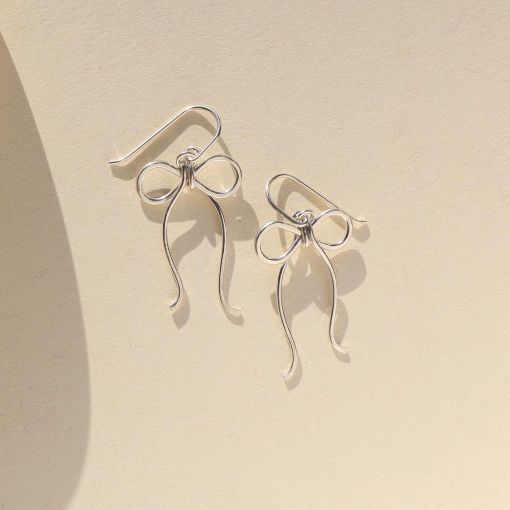 sterling silver hand shaped bow earrings on french ear wire on a light background