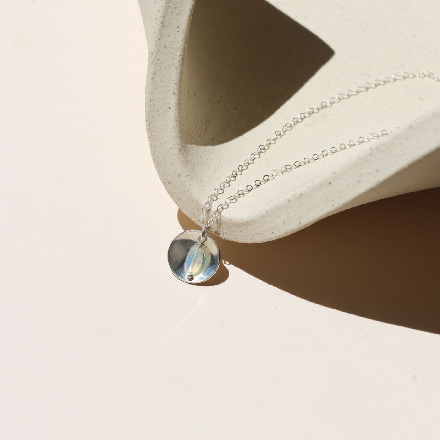 sterling silver delicate chain necklace with round charm and opal on a light dish