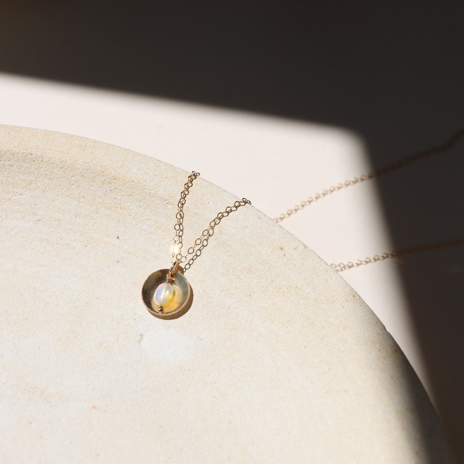 14k gold fill delicate chain necklace with opal charm and circle domed charm on a light dish