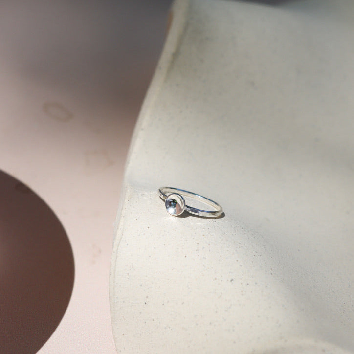 sterling silver delicate band ring with curved disc on a light dish