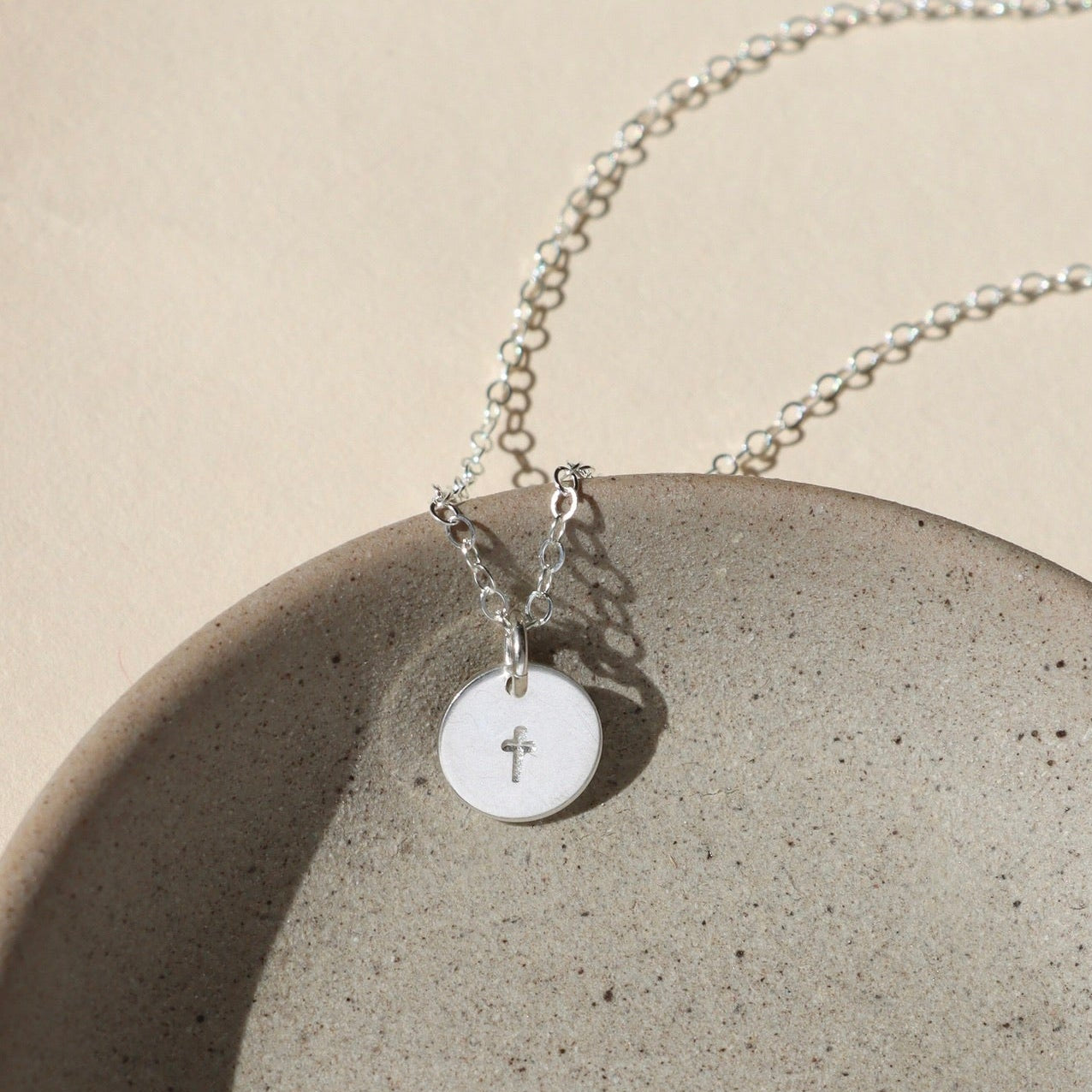 Sterling silver delicate chain necklace with a sterling silver hand stamped cross charm in the sunlight